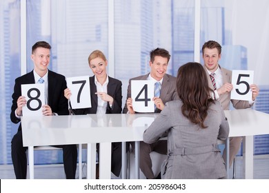 Business people showing score cards in front of female candidate during interview - Powered by Shutterstock