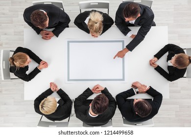 Business people sitting around empty table, business man pointing to blank copy space in the middle