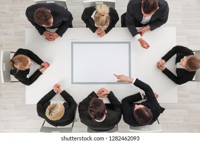 Business people sitting around empty table , copy space for text , business man pointing to blank copy space in the middle