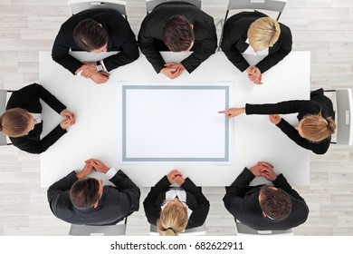 Business people sitting around empty table, business woman pointing to blank copy space in the middle