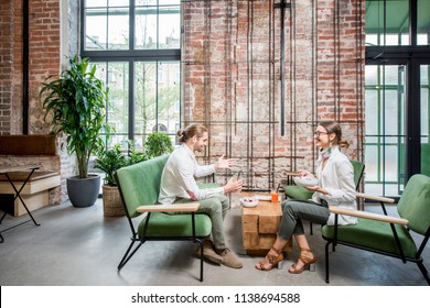 Business People Sitting On The Green Sofas During A Lunch At The Beautiful Loft Interior On The Brick Wall Background