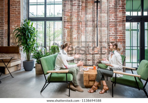 Business\
people sitting on the green sofas during a lunch at the beautiful\
loft interior on the brick wall\
background