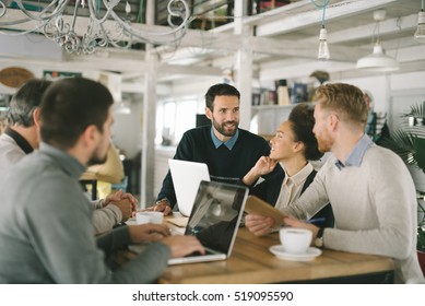Geschäftsleute in intelligenter Freizeitbekleidung diskutieren über Angelegenheiten, benutzen einen Laptop, trinken Kaffee und lächeln während der Mitarbeit im Cafe

