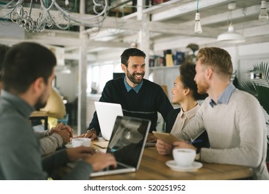 Geschäftsleute in intelligenter Freizeitbekleidung diskutieren über Angelegenheiten, benutzen einen Laptop, trinken Kaffee und lächeln während der Mitarbeit im Cafe