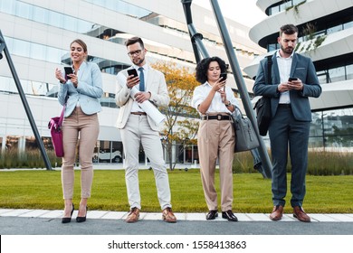 Business People Standing Outside Of Office Buildings Looking At Their Phones. 