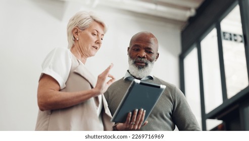 Business people, tablet and conversation working on report, reading communication or planning startup leadership strategy. Senior man, woman and discussion standing in lobby on digital tech device - Powered by Shutterstock