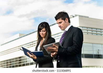 Business People Taking Notes On Tablet And Notebook Outside Of Company Building. Couple Working. Copy Space.