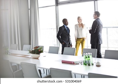 Business People Talking While Standing By Conference Table In Office