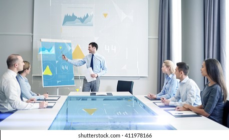 Business, People And Teamwork Concept - Group Of Smiling Businesspeople With Virtual Charts Projection Meeting On Presentation In Office