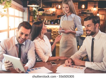 Business people are using digital tablet and smiling while having coffee break in cafe, beautiful waitress is taking order