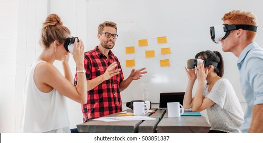 Business people using virtual reality goggles during meeting. Team of developers testing virtual reality headset and discussing new ideas to improve the visual experience. - Powered by Shutterstock