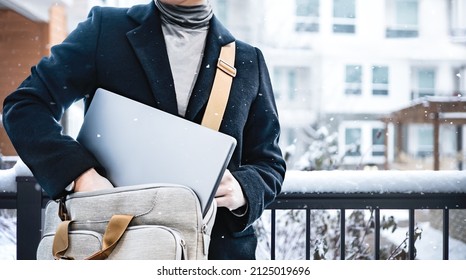 Business people wearing black coat put laptop in the suitcase after work with snow falling, standing outside the buildings. Freelance job, remote worker concept. Crop image of businessman outdoor.