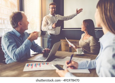 Business people are working in office. Handsome young businessman is making presentation for his colleagues, using a digital tablet and pointing to the board - Shutterstock ID 491978470