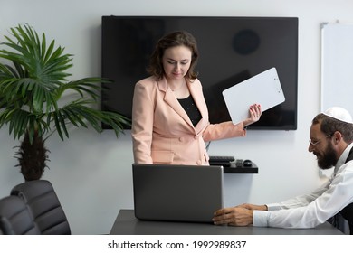 Business People Working In The Office. Business Woman Entrepreneur Using Computer Looking At Screen, Smiling Female Professional Employee Typing Email On Laptop With Jewish Man In Kippah At Workplace