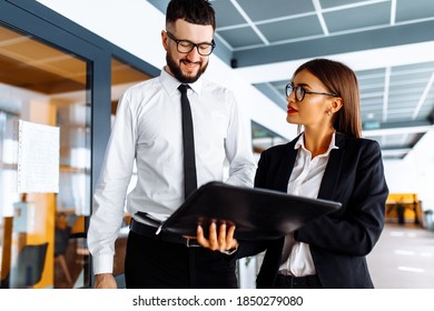 Business People, Young Man And Woman Are Walking Down The Hallway In The Office, Discussing Documents