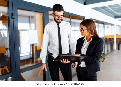 Business People, Young Man And Woman Are Walking Down The Hallway In The Office, Discussing Documents