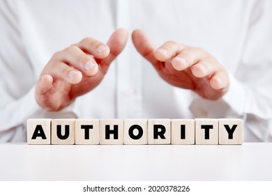 Business Person Holding His Hands Over The Wooden Cubes With The Word Authority. Power And Leadership In Business Concept.