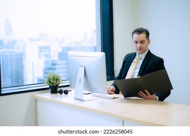 Business Person Looking At Hard Copy File With Intense And Serious Emotion At Desk Beside Window With Hugh Building View In Office Room In Capital City.