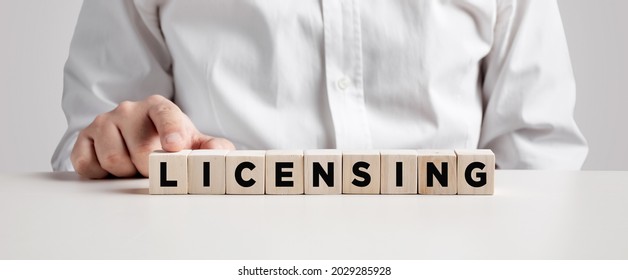 Business person presses his finger on the wooden cubes with the word licensing. Copyright protection law license property rights.  - Shutterstock ID 2029285928