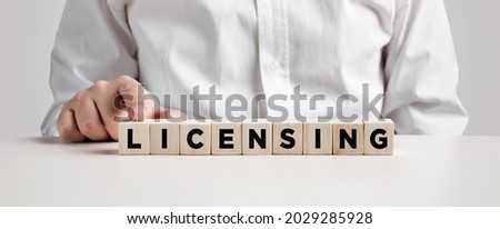 Business person presses his finger on the wooden cubes with the word licensing. Copyright protection law license property rights. 