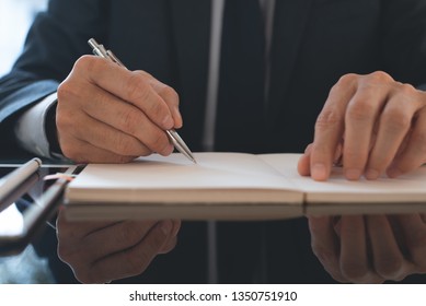 Business plan concept. Businessman, project manager in black suit planning his work on paper notebook with digital tablet on desk in modern office, close up - Shutterstock ID 1350751910