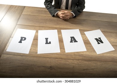 Business plan and strategy concept with a businessman sitting at a desk with the word Plan spelt out in letters on individual pages of paper spread out in front of him. - Shutterstock ID 304881029