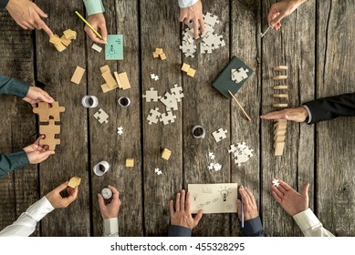 Business planning and brainstorming concept with a team of ten businessmen organizing strategy while holding puzzle pieces, writing down ideas on paper and rearranging wooden blocks, top view.