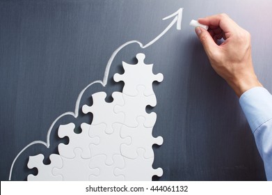 Business planning. Concept image of developing growth strategy.
Steps shaped jigsaw puzzle. Drawing arrow on blackboard.

