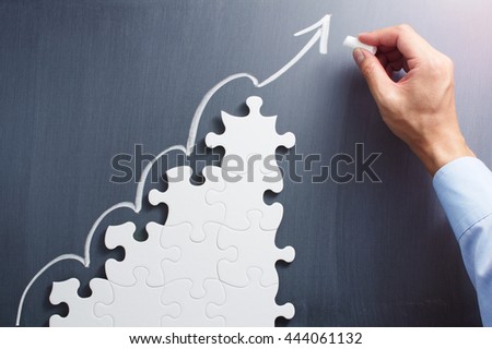 Business planning. Concept image of developing growth strategy.
Steps shaped jigsaw puzzle. Drawing arrow on blackboard.

