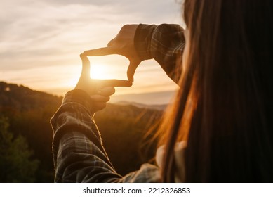 Business planning, strategy and vision concept. Close-up of young female making frame gesture with amazing beautiful sunset in mountains. Woman capturing sunrise. Copy space for promotion content