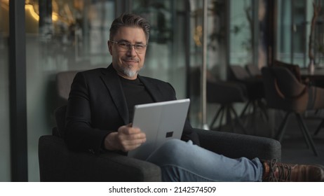 Business portrait - businessman using tablet computer in office lobby or on cafe terrace. Happy middle aged man, entrepreneur working online. - Shutterstock ID 2142574509