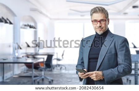 Business portrait - confident businessman in office. Trustworthy older man in his 50s with gray hair wearing glasses and jacket. Copy space.