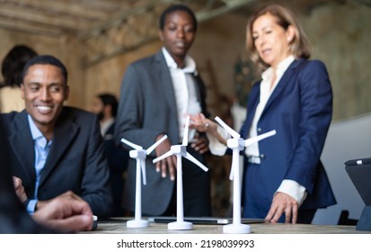 Business Portrait Of Engineers Team Discussing About A Wind Power Plant Project.  Models Of A Wind Turbine On The Table. Ecology Theme And New Sustainable Energy Concept