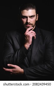 Business Portrait Of A White Caucasian Man In A Black Classic Suit On A Black Background. Bearded Man Looks Confident Eyes.