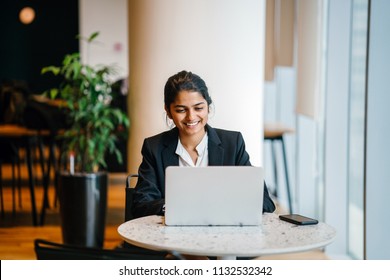 Business Portrait Of A Young Indian Asian Woman Professional In A Suit Sitting At A Desk In Her Office. She Is Replying Emails And Working On Her Notebook Computer.