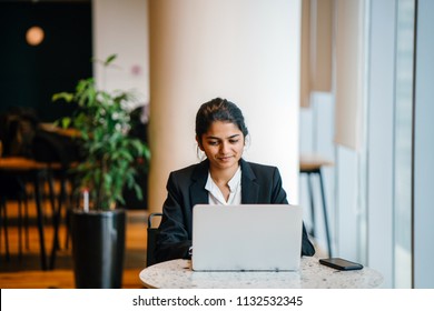 Business Portrait Of A Young Indian Asian Woman Professional In A Suit Sitting At A Desk In Her Office. She Is Replying Emails And Working On Her Notebook Computer.