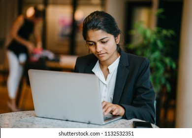 Business Portrait Of A Young Indian Asian Woman Professional In A Suit Sitting At A Desk In Her Office. She Is Replying Emails And Working On Her Notebook Computer.