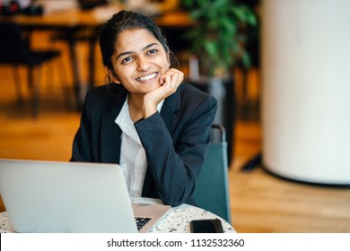 Business portrait of a young Indian Asian woman professional in a suit sitting at a desk in her office. She is replying emails and working on her notebook computer.