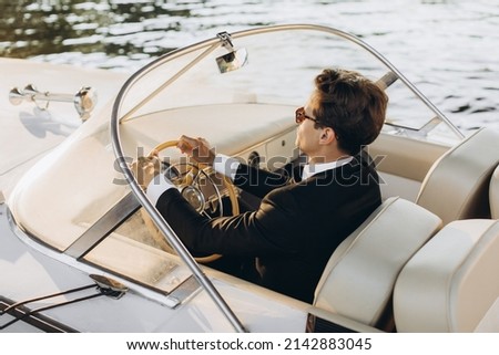 Business portrait of young man in suit and sunglasses posing on a yacht in a daylight sun