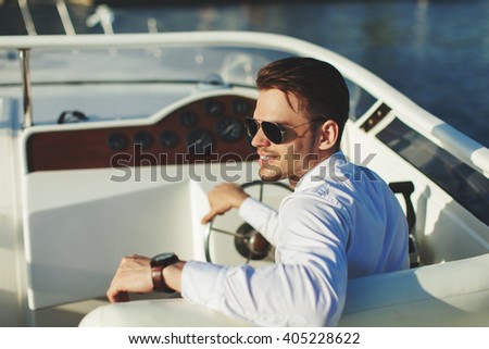 Business portrait of young smiling stylish man in suit and sunglasses driving yacht