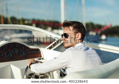 Business portrait of young stylish man in suit and sunglasses driving luxury motorboat yacht