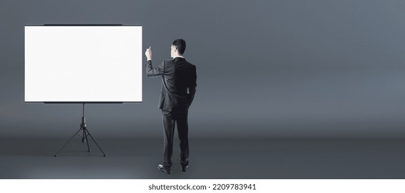 Business Presentation Concept With Man In Black Suit Back View In Front Of Blank White Flip Chart With Place For Your Logo Or Text On Dark Wall Background, Mock Up