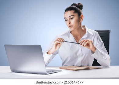 Business Process And Job Concept With Pretty Young Woman Sitting At White Desk, Looking At Laptop Screen And Carrying Pencil In Hands On Abstract Light Blue Wall Background