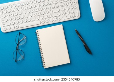 Business Productivity Setup: Top view shot featuring keyboard, mouse, spiral notepad, pen, glasses on blue backdrop. Blank area for text or ads - Powered by Shutterstock