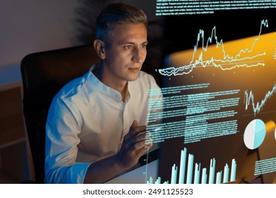 Business Professional Analyzing Data on Transparent Screen, Focused Man Interpreting Financial Graphs, Charts, and Diagrams. High-Tech Office Environment, Night Work, Innovation, and Technology. - Powered by Shutterstock