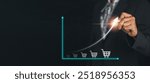 A business professional drawing an upward graph with shopping cart icons, symbolizing sales growth and business success on a dark background.