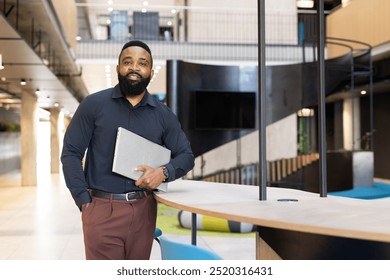 Business professional holding laptop, standing confidently in modern office lobby, copy space. corporate, executive, technology - Powered by Shutterstock