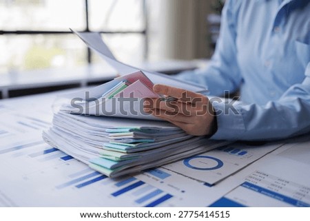Business professional is organizing multiple documents and analyzing financial reports with charts and graphs, demonstrating efficient workflow and meticulous data management