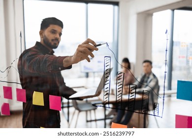 Business professional presenting data analysis on transparent board during meeting. Team collaboration with bar charts and sticky notes in modern office setting. - Powered by Shutterstock