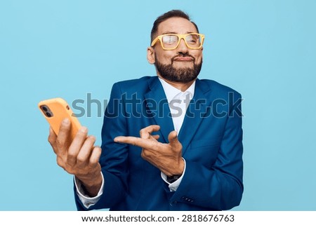 A business professional stands against a solid blue background, isolated and vibrant. The man exudes confidence, pride, and approachability, as he holds a phone and makes a bold gesture.